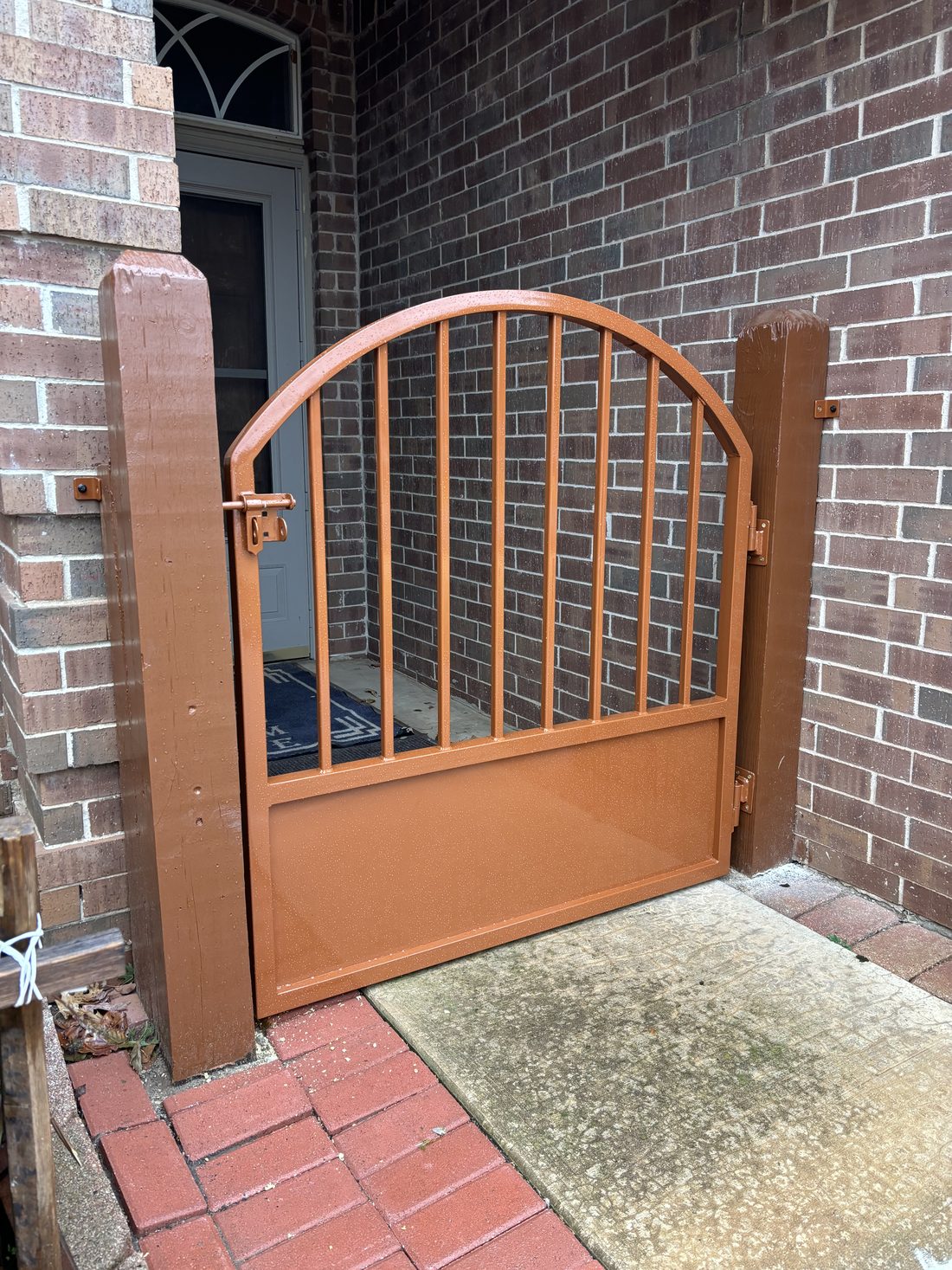Copper-tone metal entry gate installed against brick.